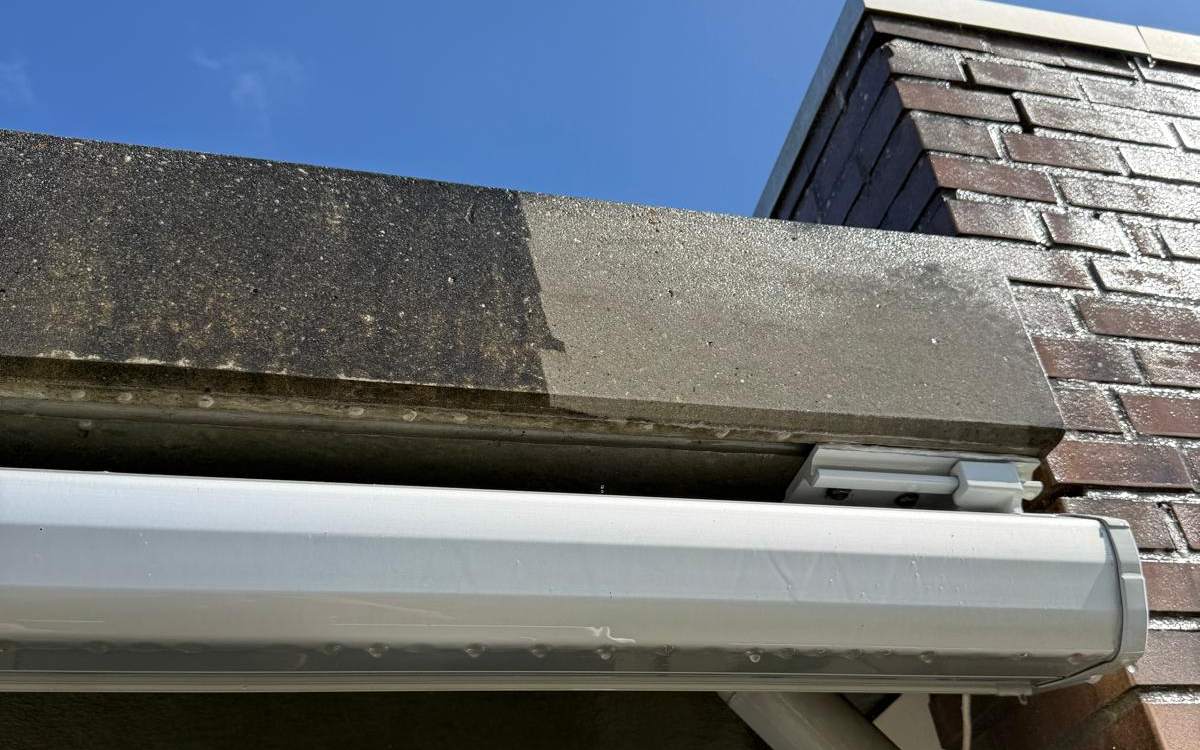 Betonnen dakrand boven een entree: links vuil, rechts gereinigd