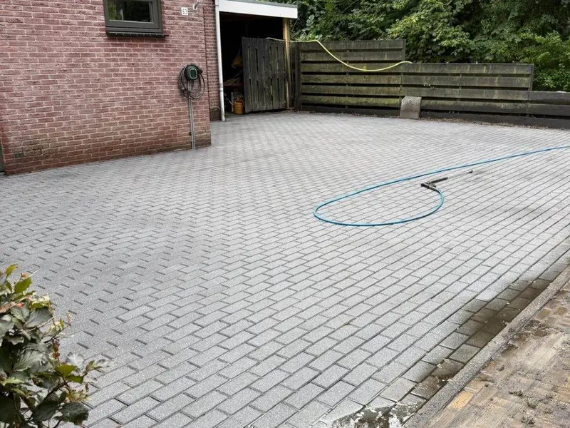 Grijze oprit van betonklinkers naast een bakstenen woning